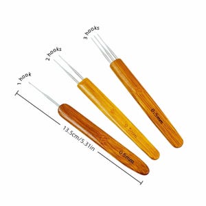 May include: Three dreadlock crochet hooks with bamboo handles, each labelled 0.5mm. The set includes a single hook, a double hook, and a triple hook. A measurement line indicates a total length of 13.5cm for the tools.