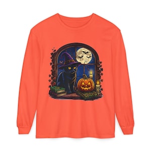 May include: A bright orange long-sleeve shirt featuring a graphic print of a black cat wearing a purple witch hat, sitting by a window with a full moon, bats, a jack-o'-lantern, lit candles, and stacked books in a dark, nocturnal setting.