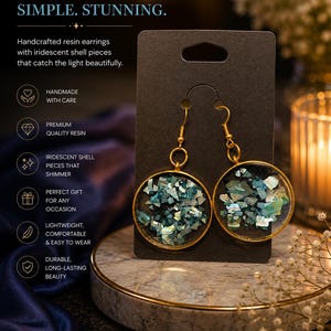 Puede incluir: Un par de pendientes redondos de resina con fragmentos de concha iridiscente azul y verde incrustados en marcos circulares dorados. Los pendientes se presentan en una tarjeta negra con el texto SHIMMER. SIMPLE. STUNNING. y detalles del producto.