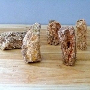 May include: A collection of rough-hewn, irregularly shaped stones in shades of brown and tan. The stones are arranged on a light-colored wooden surface, with a pale blue background.