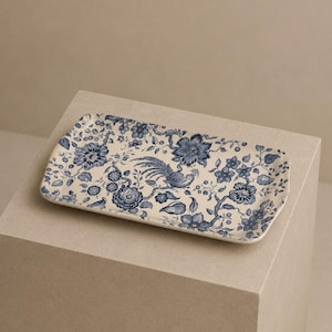 Op de afbeelding: Een rechthoekig keramieken dienblad met een crèmekleurige basis en een gedetailleerd blauw bloemenpatroon. Het ontwerp bevat diverse bloeiende bloemen, bladerrijke takken en een centraal vogelmotief, uitgevoerd in een klassiek blauw-wit kleurenschema.