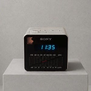 以下が含まれることがあります： シルバーとブラックのソニー製デジタル目覚まし時計付きラジオ。正方形の前面パネルには、明るい青色のデジタル数字で11:35と表示されており、その下にはFMおよびAMラジオの周波数スケールと、斜めに配置されたチューニング針が表示されています。