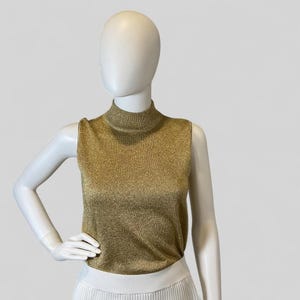 May include: A sleeveless mock neck top in a shimmering gold metallic knit fabric. The garment features a fitted silhouette with a high neckline and a textured, glittery finish throughout the material, displayed on a white mannequin torso.