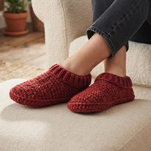 Puede incluir: Un par de zapatillas de punto grueso en color rojo oscuro con un patrón tejido texturizado y un cuello acanalado. Las zapatillas están confeccionadas con hilo grueso y tienen un diseño de punta redondeada, ofreciendo un aspecto acogedor.