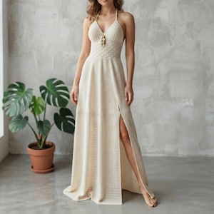 May include: A floor-length cream-colored crochet dress featuring a V-neckline, thin spaghetti straps, a textured bodice with a central decorative bead detail, and a high side slit that extends from the mid-thigh to the hem of the skirt.