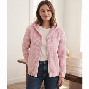 May include: A light pink hooded cardigan with a textured waffle-knit pattern, featuring long sleeves, a ribbed hem, and a single button closure at the neckline, worn over a plain white t-shirt and dark blue denim jeans.