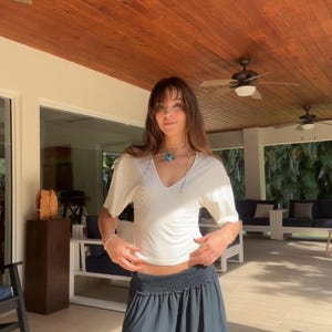 May include: A white short-sleeved V-neck top paired with a dark gray maxi skirt featuring a wide, gathered elastic waistband. The top is fitted with short sleeves, while the skirt has a long, flowing silhouette that reaches the ankles.