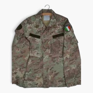 May include: A long-sleeved camouflage jacket featuring a multi-coloured pattern of green, brown, and tan. The jacket includes a collar, two chest pockets with dark brown rectangular patches, and a circular patch on the left sleeve with the text ITALIA.