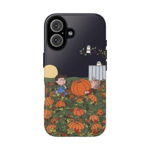 May include: A dark-colored smartphone case featuring a Peanuts-themed illustration of two characters in a pumpkin patch at night. The scene includes a large orange pumpkin, a yellow moon, green foliage, and two small white ghosts on a fence.