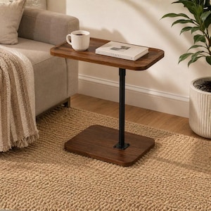 May include: A C-shaped side table with a dark wood grain rectangular top and base, connected by a single black metal vertical support pole. A white ribbed ceramic mug and a white book titled Cereal are placed on the table surface.
