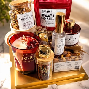 May include: A gift set containing a jar of Saffron Bloom herbal tea, a red pouch of Epsom and Himalayan bath salts, a red glass candle with GIB label, a gold tea infuser, a spray bottle of Rouge No. 540, and a container of roasted nut mix.