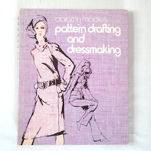May include: A rectangular book titled Dorothy Moore's Pattern Drafting and Dressmaking with a purple and white grid background. The cover features black line-art illustrations of two figures wearing clothing, one standing and one sitting.