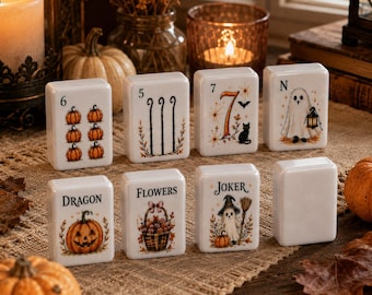 May include: A set of eight white rectangular mahjong tiles featuring Halloween-themed illustrations, including pumpkins, ghosts, a black cat, and a basket of flowers, with text labels such as 6, 5, 7, N, Dragon, Flowers, and Joker printed on the front.