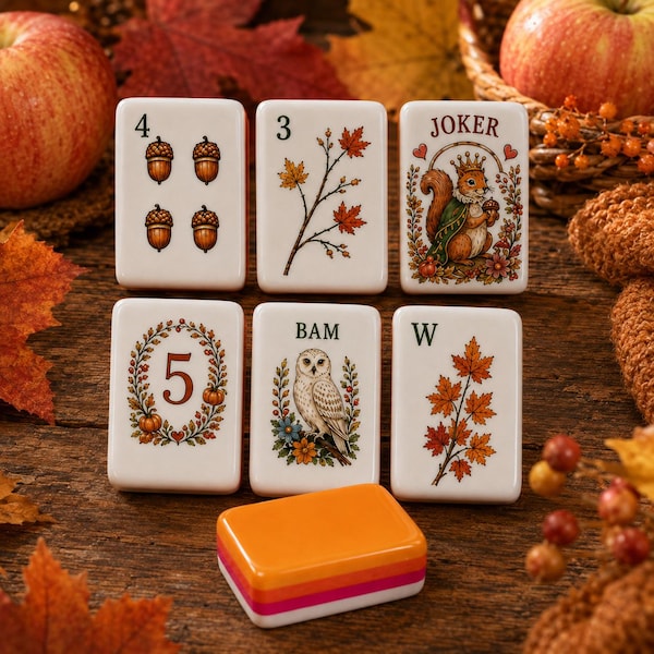 May include: Six rectangular white tiles with autumn-themed illustrations including acorns, maple leaves, a squirrel labelled JOKER, a number 5 surrounded by a wreath, an owl, and a W, plus one solid orange tile stacked on a wooden surface.