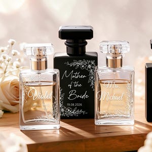 May include: Four rectangular perfume bottles with black or clear glass and black caps. Two clear bottles feature white floral engravings and the names Violet and Michael. The central black bottle is engraved with Mother of the Bride and 19.08.2026.
