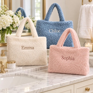 Puede incluir: Tres bolsos tote rectangulares de material texturizado y esponjoso en color crema, azul y rosa. Cada bolso tiene dos asas superiores y un nombre bordado en el centro: Emma en el bolso crema, Chloe en el azul y Sophia en el bolso rosa.