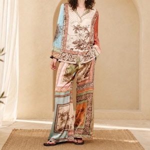 May include: A long-sleeve button-down shirt and matching wide-leg trousers featuring a multi-colored patchwork print. The design incorporates various panels with tropical landscape scenes, palm trees, floral motifs, and geometric borders in shades of blue, cream, brown, and pink.