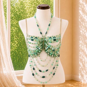 May include: A beaded body chain top featuring a butterfly-inspired design crafted from various shades of green and mint beads. The garment includes delicate gold-toned metal chains, a halter-style neckline, and multiple draped strands of beads.