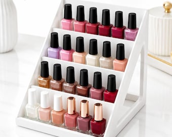 May include: A white tiered display rack holding twenty-four glass nail polish bottles. The bottles feature black caps, except for the bottom row which has metallic gold caps. The colors range from light pinks and nudes to deep reds and glitters.