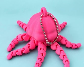 May include: A bright pink octopus-shaped fidget keychain with articulated, segmented tentacles and a silver-toned metal ball chain. The text OCTOPUS CLICKER Fidget Keychain is printed in dark letters above the object.