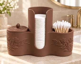 May include: A brown bathroom vanity organizer featuring a central cylindrical holder for cotton rounds, a lidded container on the left, and an open compartment on the right for cotton swabs, all decorated with embossed floral patterns.