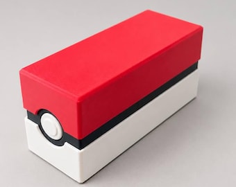 May include: A rectangular storage box featuring a red top half and a white bottom half, separated by a thin black horizontal band. A circular white button is centered on the front black band, mimicking the design of a classic spherical container.