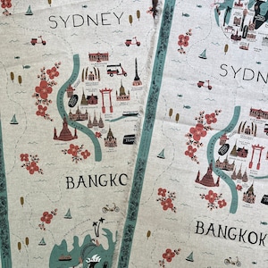 May include: Two fabric tea towels with a map design. The top towel features a map of Sydney, Australia, with the words "SYDNEY!" printed in black. The bottom towel features a map of Bangkok, Thailand, with the words "BANGKOK" printed in black. Both towels have a light beige background with a blue and green map design.