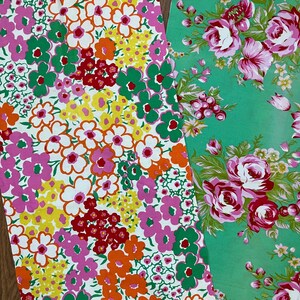 May include: Two floral fabric swatches. One features a white background with a vibrant mix of pink, orange, yellow, and green flowers. The other has a green background with pink and red roses and green leaves. The fabrics are likely for sewing or crafting.