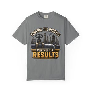 May include: A grey short-sleeve t-shirt featuring a graphic print of an industrial pipeline with a large valve. Above the graphic is the text "CONTROL THE PROCESS" and below it is the text "CONTROL THE RESULTS" in bold, yellow, block lettering.
