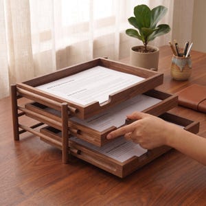 May include: A three-tiered dark wood document tray organizer with a natural grain finish. Each rectangular tray holds white paper sheets with printed text. The structure features vertical support posts and a cutout handle on each tray front.
