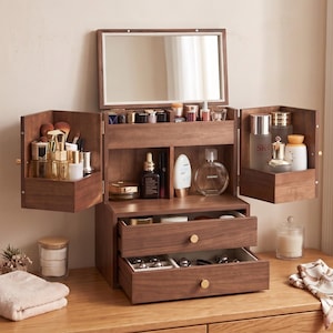 May include: A dark wood vanity organizer featuring a flip-top mirror, two side-opening cabinets with shelves, and two lower drawers with gold-toned knobs. The unit is filled with various skincare bottles, makeup brushes, and cosmetic containers.
