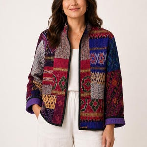 Könnte beinhalten: Eine langärmelige Jacke mit einem lebendigen Patchwork-Design aus verschiedenen geometrischen und floralen Mustern in Rot-, Blau-, Lila- und Gelbtönen. Die Jacke hat einen Stehkragen, einen schwarzen Saum entlang der Vorderseite und Ärmelbündchen.