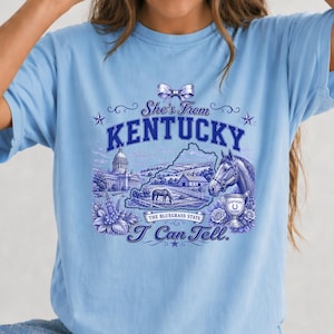 A blue t-shirt with a graphic design featuring a horse, a state map, and various decorative elements.