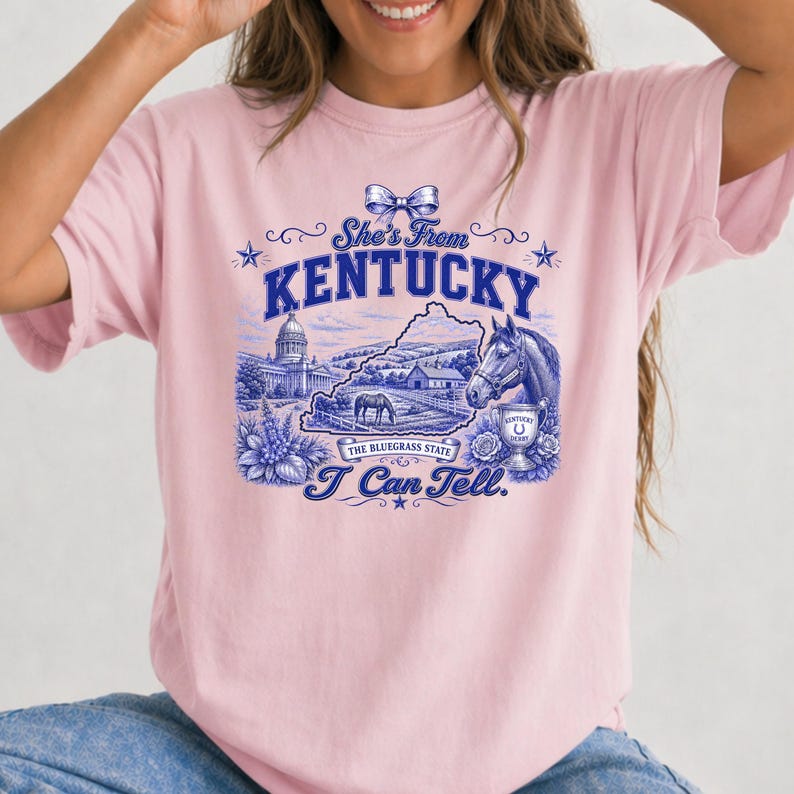 A woman wearing a pink t-shirt with a graphic design depicting various elements associated with Kentucky, such as a horse, state building, and text.