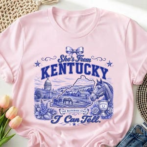 A pink t-shirt with a graphic design featuring a horse, flowers, and the text "She's from Kentucky" and "I can tell."