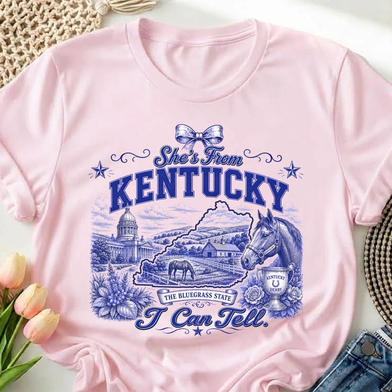 A pink t-shirt with a graphic design featuring a horse, flowers, and the text "She's from Kentucky" and "I can tell."