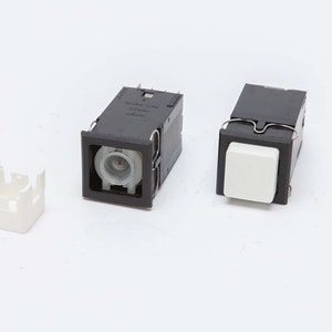May include: An assortment of black and white electrical components, including two rectangular push-button switches with white buttons and a separate white plastic housing. The components are set against a plain white background.