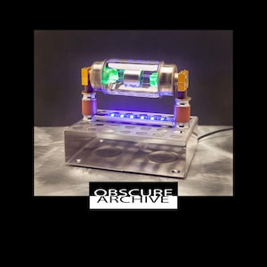 May include: A unique, illuminated art piece featuring a clear glass tube with green internal components, supported by gold-colored hardware and a silver metal base. The base has blue LED lights. The text "OBSCURE ARCHIVE" is displayed in a black and white box.