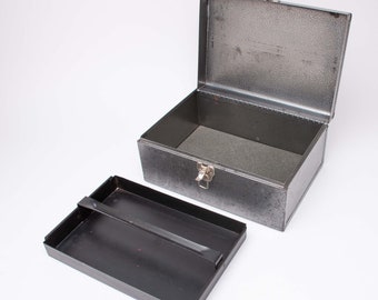 May include: A vintage metal toolbox with a hinged lid and a separate tray. The toolbox is dark gray with a textured finish and a silver latch. The tray is black with a handle. The toolbox is open, revealing the interior.