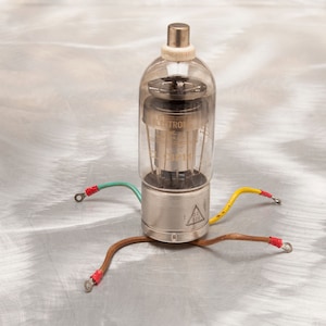 May include: A vintage vacuum tube with a clear glass bulb and a silver metal base. The tube has internal components visible through the glass and is connected to wires with red, green, and yellow insulation. The tube is labeled "ELEKTRON" and "EL3P14".