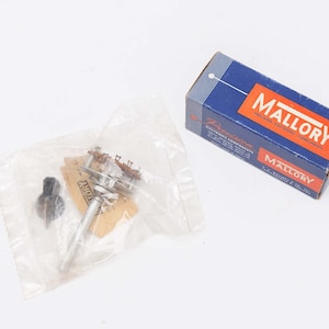 May include: An assortment of electronic components, including a potentiometer and a black knob, are displayed. The components are packaged in a clear plastic bag and a blue and red Mallory box. The box has the word "MALLORY" in large white letters.