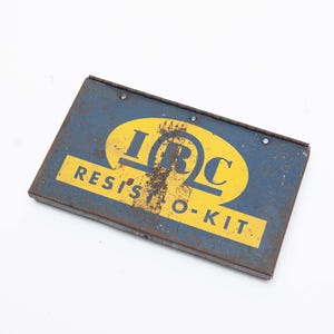 May include: A rectangular, blue metal box with the text "IRC RESIST-O-KIT" in yellow. The box has a distressed appearance, suggesting age or wear. The text is in a bold, sans-serif font.