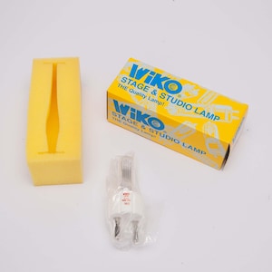 May include: A yellow box with the text "WIKO STAGE & STUDIO LAMP" in blue and white, along with a yellow foam insert and a packaged light bulb. The box is yellow with blue text.