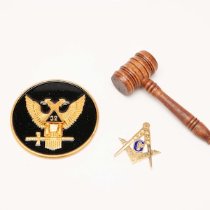 May include: An assortment of Masonic items, including a wooden gavel, a gold-colored compass and square emblem with a blue "G", and a black and gold emblem with a double-headed eagle and the number "32".