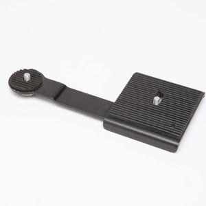 May include: Black camera quick release plate with a textured surface and a screw mount. The plate has a rectangular base with a ridged pattern and a connecting arm with a circular mount.