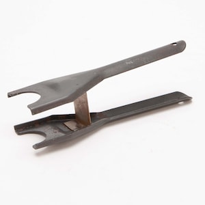 May include: A dark gray metal tool with a unique design. It features two forked ends connected by a central support and a small metal piece. The tool has a hole at the end of one of the arms.