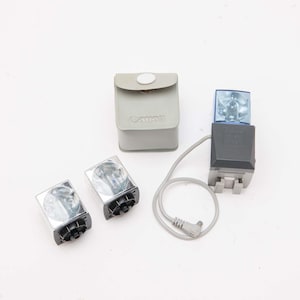 May include: A collection of Canon camera accessories, including two flash units, a flash unit with a blue cover, and a gray carrying case. The flash units have a black base and a silver reflector. The carrying case is gray.