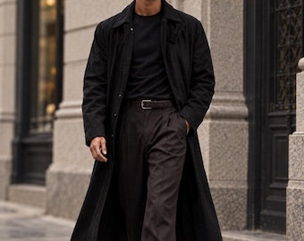 以下が含まれることがあります： 黒いロングトレンチコート、黒いTシャツ、ベルト付きのダークブラウンのパンツ。ダークカラーのサングラスと黒いレザーのローファーを着用。構造的な襟と長袖が特徴的なスタイルで、ストレートレッグのパンツを合わせています。