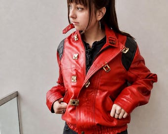 以下が含まれることがあります： 黒いキルティングのショルダーパネル、ゴールドトーンの金属製バックル、フロントジッパーを備えた鮮やかな赤のレザージャケット。ジャケットにはバックルストラップ付きのハイカラー、長袖、ウエストにギャザー入りの伸縮性のある裾が施されています。