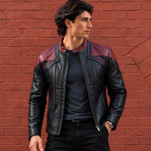 Puede incluir: Una chaqueta de cuero negra con paneles de hombro en color rojo oscuro, cuello alto con cierre de botón a presión, cremallera frontal completa y costuras verticales. La chaqueta se lleva sobre una camiseta gris oscuro y pantalones negros.